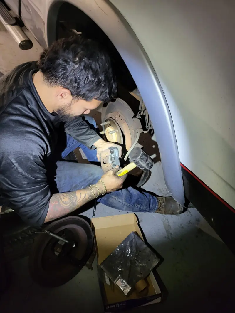 Mechanic replacing brake calipers on a pickup truck at night